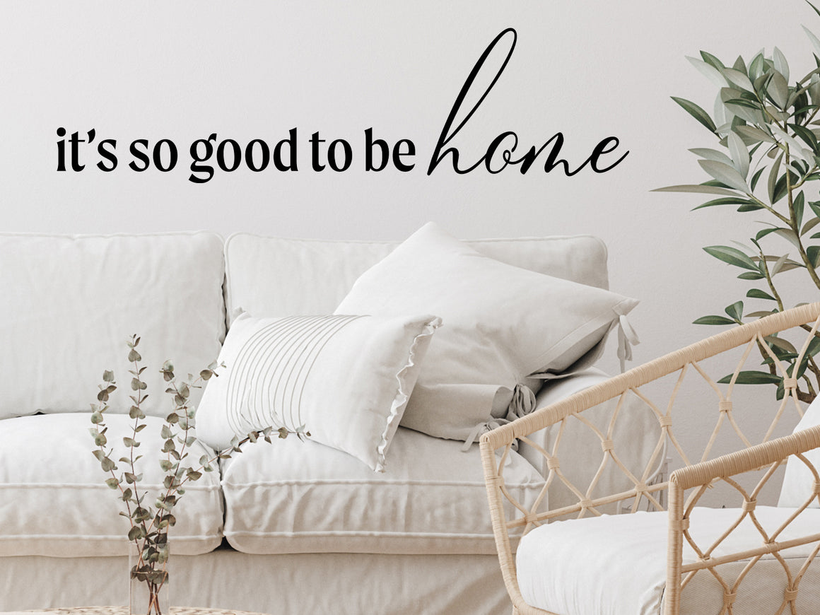 Living room wall decals that say ‘It's So Good To Be Home’ in a script font on a living room wall. 