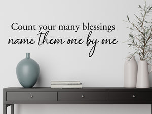 Living room wall decals that say ‘Count Your Many Blessings Name Them One By One’ in a script font on a living room wall.