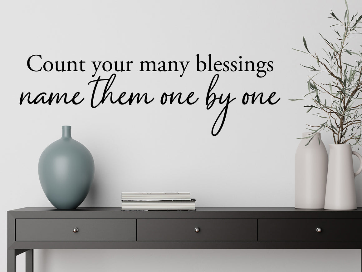 Living room wall decals that say ‘Count Your Many Blessings Name Them One By One’ in a script font on a living room wall.