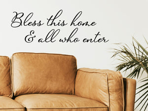 Living room wall decals that say ‘Bless This Home And All Who Enter’ in a cursive font on a living room wall. 