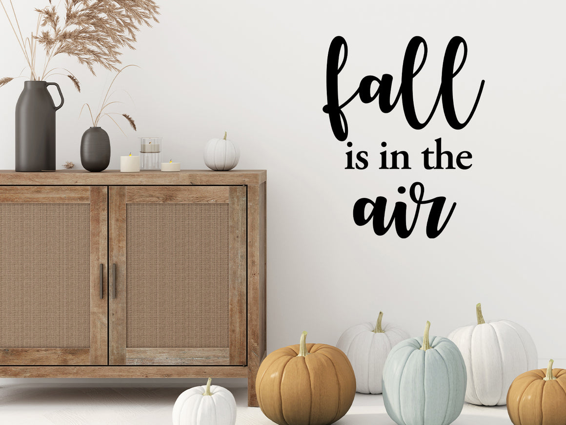 Living room wall decals that say ‘Fall Is In The Air’ in a bold font on a living room wall. 