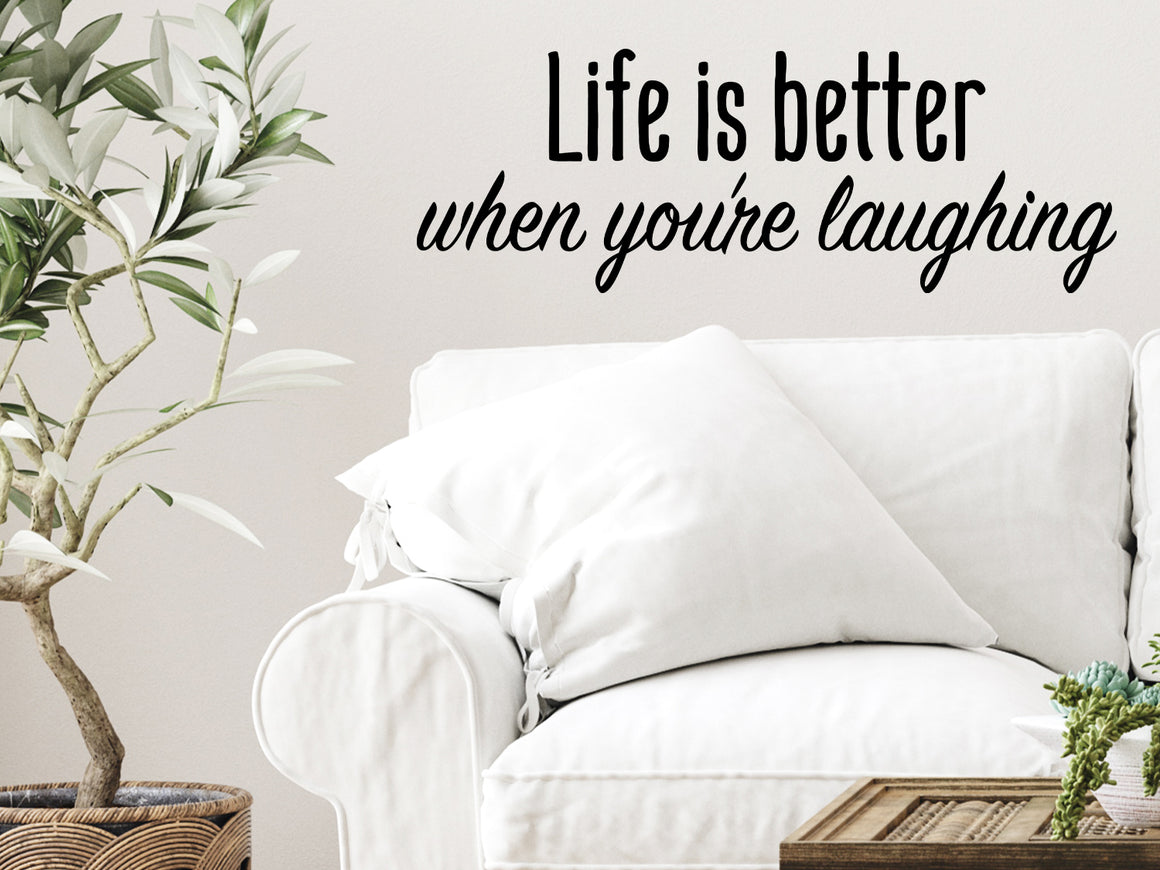 Living room wall decals that say ‘Life Is Better When You're Laughing’ in a script font on a living room wall. 