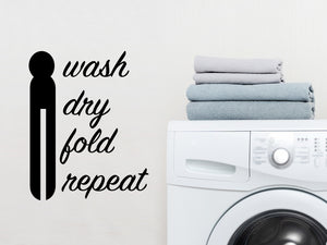 Laundry room wall decal that says ‘Wash Dry Fold Repeat (ClothesPin)’ in a cursive font on a laundry room wall.