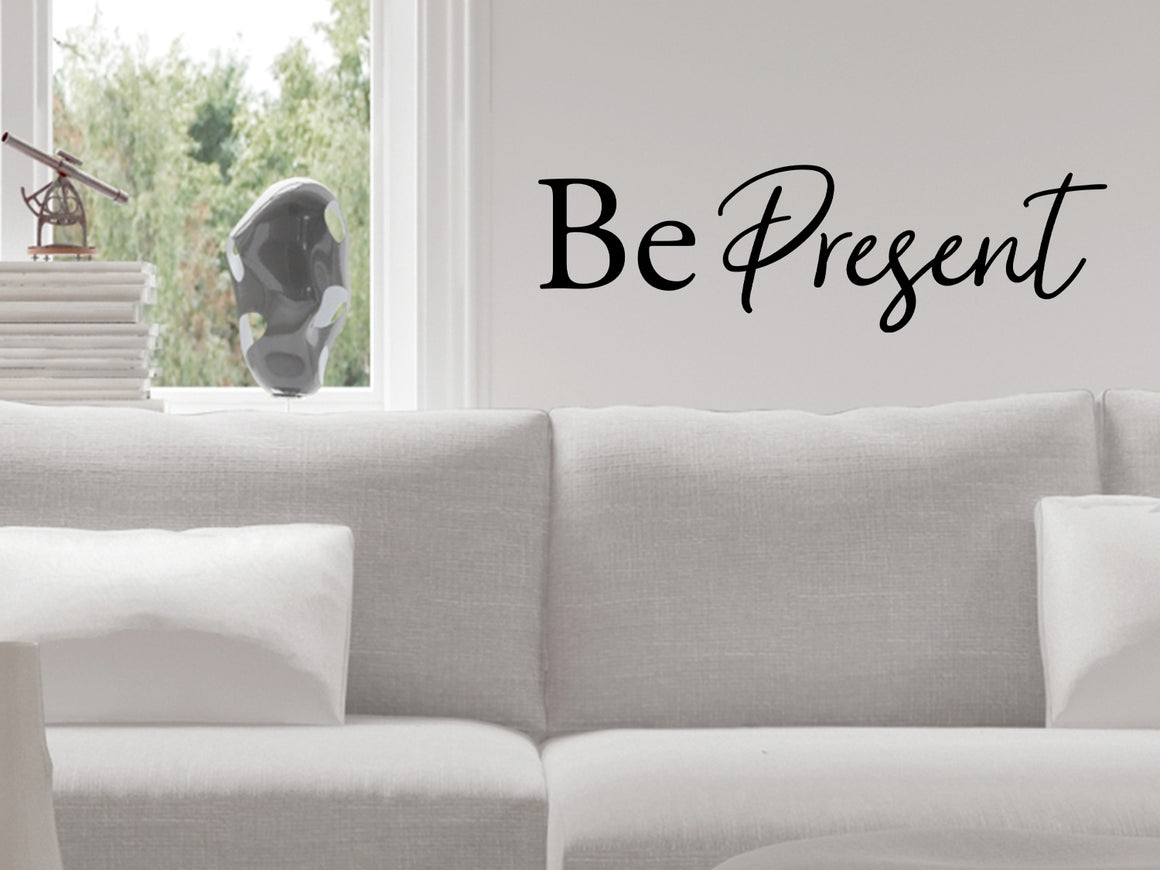 Living room wall decals that say ‘Be Present’ in a script font on a living room wall. 