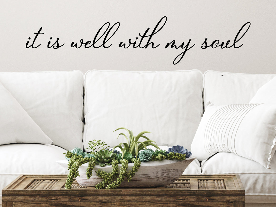 Living room wall decals that say ‘It Is Well With My Soul’ in a cursive font on a living room wall. 