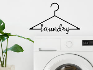 Laundry room wall decal that says ‘Laundry (Clothes Hanger)' in a Script font on a laundry room wall.