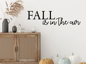 Living room wall decals that say ‘Fall Is In The Air’ in a script font on a living room wall. 