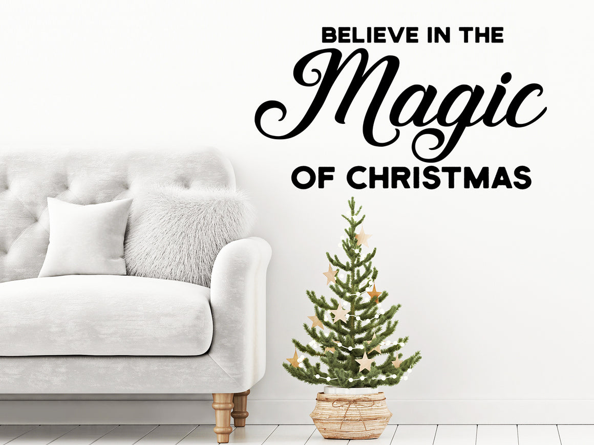 Living room wall decals that say ‘Believe In The Magic Of Christmas’ in a script font on a living room wall. 
