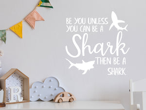 Wall decal for kids in a white color that says ‘Always Be You Unless You Can Be A Shark’ on a kid’s room wall. 