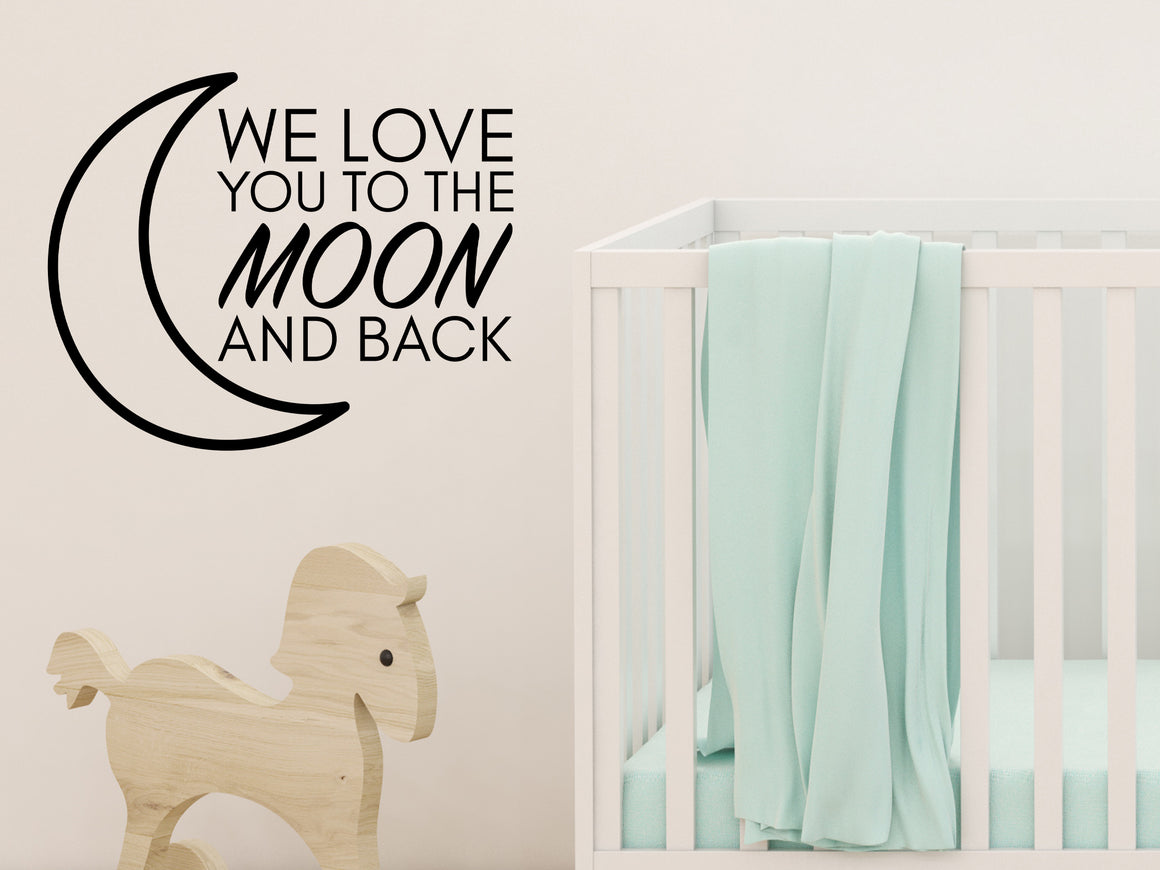 Wall decal for kids in a black color that says ‘We Love You To The Moon And Back’ in a print font  on a kid’s room wall. 