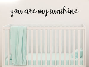 Wall decal for kids in a black color that says ‘You Are My Sunshine’ in a cursive font on a kid’s room wall. 