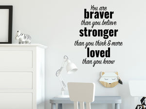 Wall decal for kids in a black color that says ‘You Are Braver Than You Believe’ in a dual font on a kid’s room wall. 