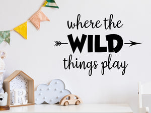 Wall decal for kids in a black color that says ‘Where The Wild Things Play’ with an arrow design on a kid’s room wall. 