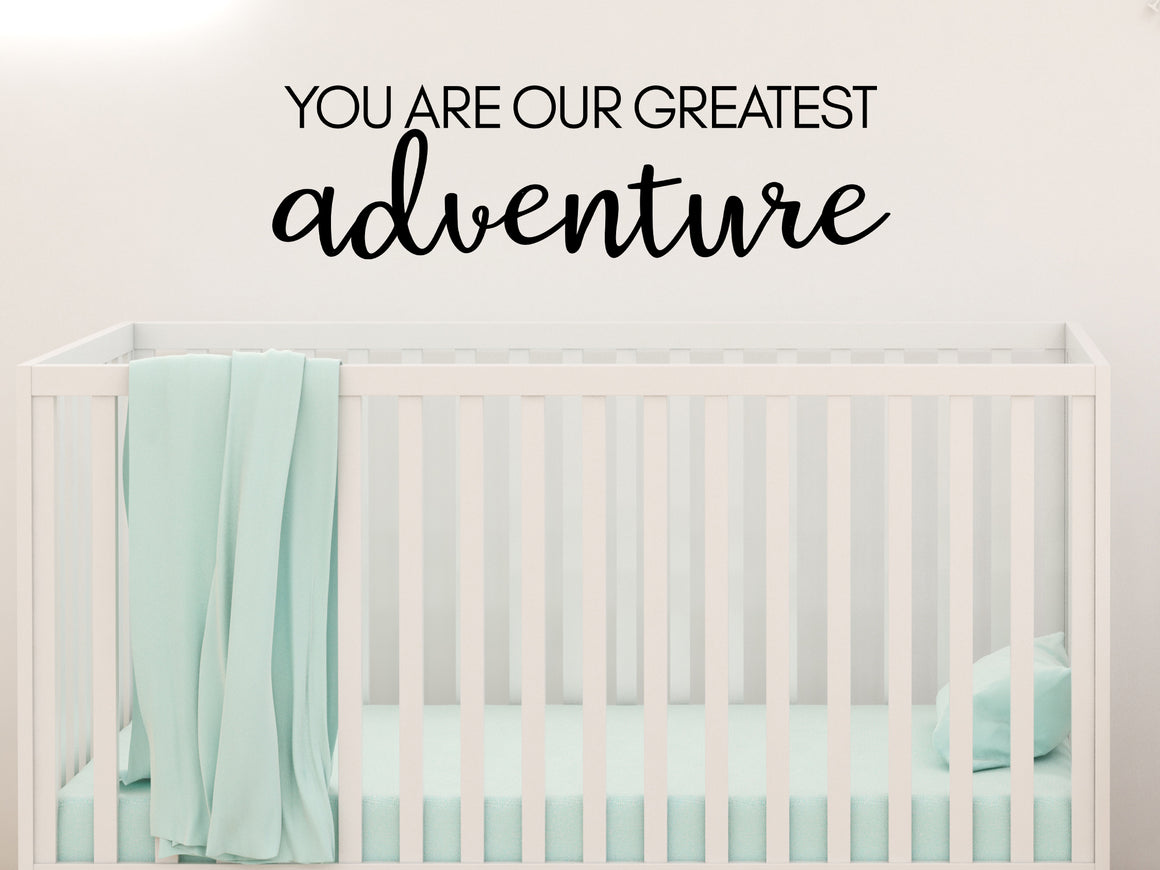 Wall decal for kids in a black color that says ‘You Are Our Greatest Adventure’ in a script font on a kid’s room wall. 