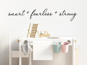 Wall decal for kids in a black color that says ‘Smart Fearless Strong’ in a cursive font on a kid’s room wall. 