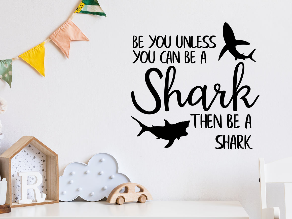 Wall decal for kids in a black color that says ‘Always Be You Unless You Can Be A Shark’ on a kid’s room wall. 