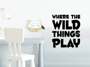 Wall decal for kids in a black color that says ‘Where The Wild Things Play’ in a bold font on a kid’s room wall. 