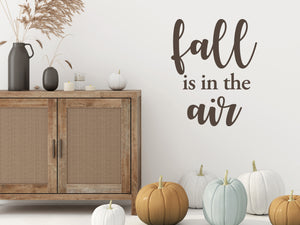 Living room wall decals that say ‘Fall Is In The Air’ in brown and a bold font on a living room wall. 