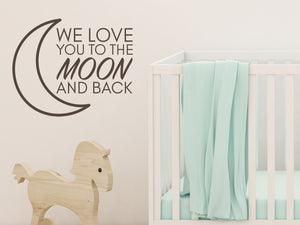 Wall decal for kids in a brown color that says ‘We Love You To The Moon And Back’ in a print font  on a kid’s room wall. 