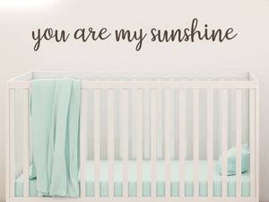 Wall decal for kids in a brown color that says ‘You Are My Sunshine’ in a cursive font on a kid’s room wall. 