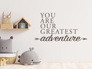 Wall decal for kids in a brown color that says ‘You Are Our Greatest Adventure’ with an arrow design on a kid’s room wall. 