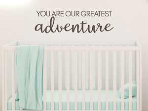 Wall decal for kids in a brown color that says ‘You Are Our Greatest Adventure’ in a script font on a kid’s room wall. 
