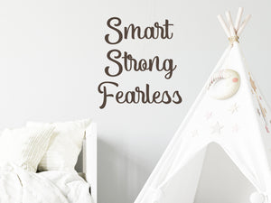 Wall decal for kids in a brown color that says ‘Smart Strong Fearless’ in a script font on a kid’s room wall. 