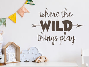 Wall decal for kids in a brown color that says ‘Where The Wild Things Play’ with an arrow design on a kid’s room wall. 