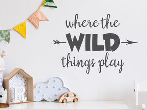 Wall decal for kids in a grey color that says ‘Where The Wild Things Play’ with an arrow design on a kid’s room wall. 