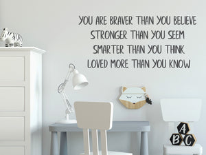 Wall decal for kids in a grey color that says ‘You Are Braver Than You Believe’ in a print font on a kid’s room wall. 