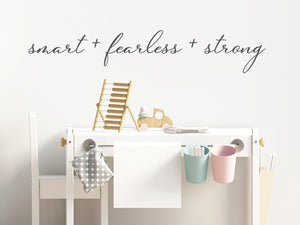 Wall decal for kids in a grey color that says ‘Smart Fearless Strong’ in a cursive font on a kid’s room wall. 