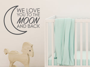 Wall decal for kids in a grey color that says ‘We Love You To The Moon And Back’ in a print font  on a kid’s room wall. 