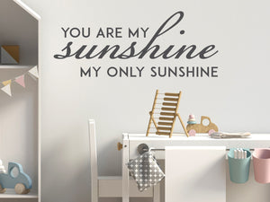 Wall decal for kids in a grey color that says ‘You Are My Sunshine’ in a script font on a kid’s room wall. 