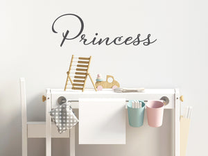 Wall decal for kids that says ‘Princess’ in grey in a cursive font on a kid’s room wall. 