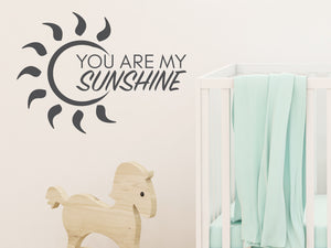 Wall decal for kids in a grey color that says ‘You Are My Sunshine’ with a sun design on a kid’s room wall. 