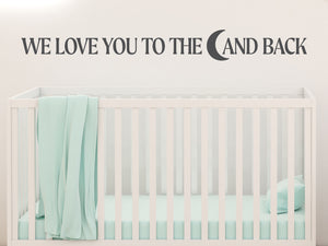 Wall decal for kids in a grey color that says ‘We Love You To The Moon And Back’ in a bold font on a kid’s room wall. 