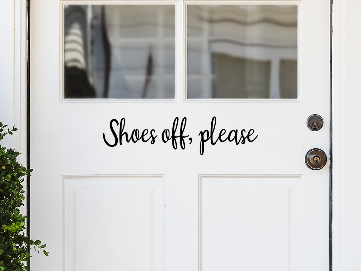 Front door decal that says, ‘shoes off please’ in a script font  on a front porch door. 