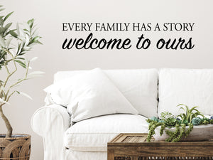 Living room wall decals that say ‘Every Family Has A Story Welcome To Ours’ in a script font on a living room wall.
