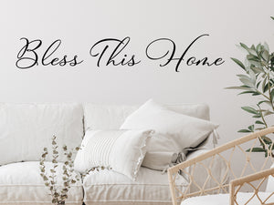 Living room wall decals that say ‘Bless This Home’ in a cursive font on a living room wall. 