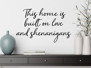 Living room wall decals that say ‘This Home Is Built On Love And Shenanigans’ in a script font on a living room wall. 