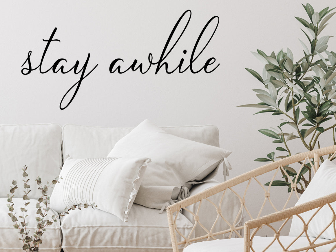 Living room wall decals that say ‘Stay Awhile’ on a living room wall in a cursive font.