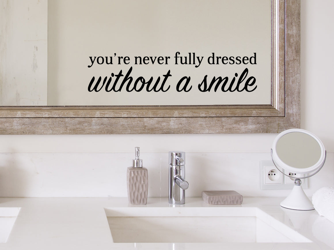 Wall decals for bathroom that say ‘You're Never Fully Dressed Without A Smile’ in a bold font on a bathroom mirror.