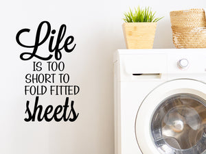 Laundry room wall decal that says ‘Life Is Too Short To Fold Fitted Sheets’ in a bold font on a laundry room wall