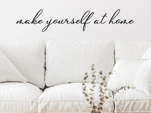 Living room wall decals that say ‘Make Yourself At Home’ in a cursive font on a living room wall. 