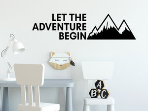 Wall decal for kids that says ‘Let The Adventure Begin’ in a print font on a kid’s room wall. 