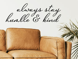 Living room wall decals that say ‘Always Stay Humble And Kind’ in a cursive font on a living room wall. 