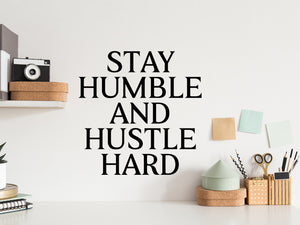 Wall decal for the office that says ‘Stay Humble And Hustle Hard’ in a print font on an office wall.