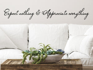 Living room wall decals that say ‘Expect Nothing Appreciate Everything’ in a cursive font on a living room wall.