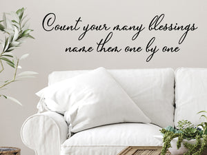 Living room wall decals that say ‘Count Your Many Blessings Name Them One By One’ in a cursive font on a living room wall.