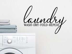 Laundry room wall decal that says ‘Laundry Wash Dry Fold Repeat’ in a script font on a laundry room wall.